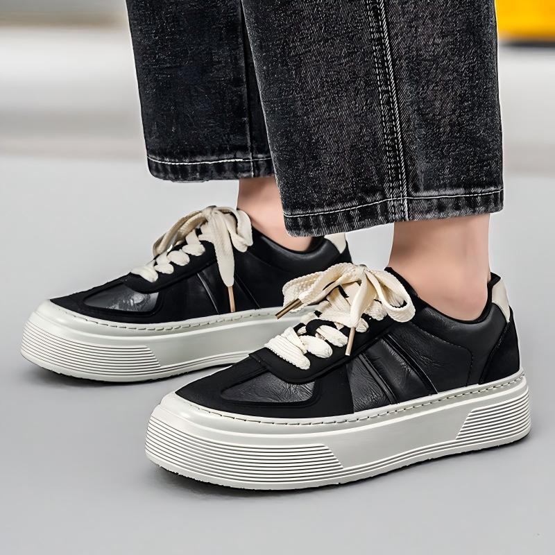 A person wearing black low-top platform sneakers with chunky off-white soles and light beige laces, paired with dark gray jeans.