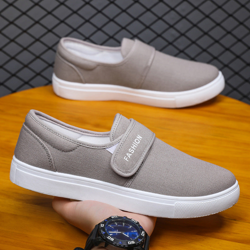 Gray slip-on shoes with white soles on a wooden surface, held by a person wearing a black watch.