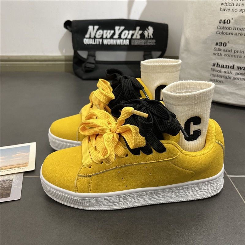 Yellow sneakers with black shoelaces on a gray surface, with 'New York' branded bag in the background.