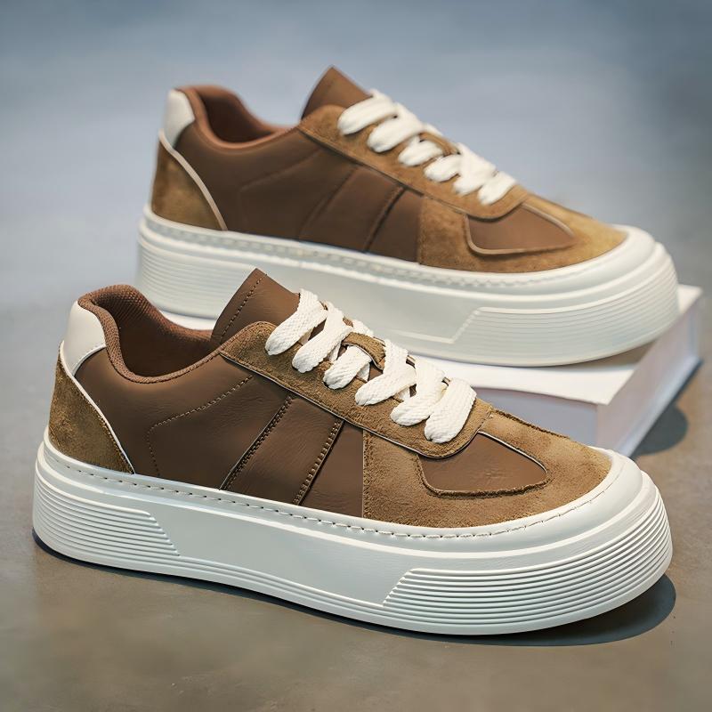 A pair of low-top platform sneakers in brown suede and leather with chunky white soles and white laces, displayed on a gray surface with one shoe resting on a white box.