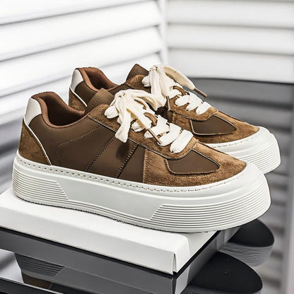 A pair of low-top platform sneakers in brown suede and smooth brown panels with chunky white soles and white laces, displayed on a white shoebox against a modern gray and white background.