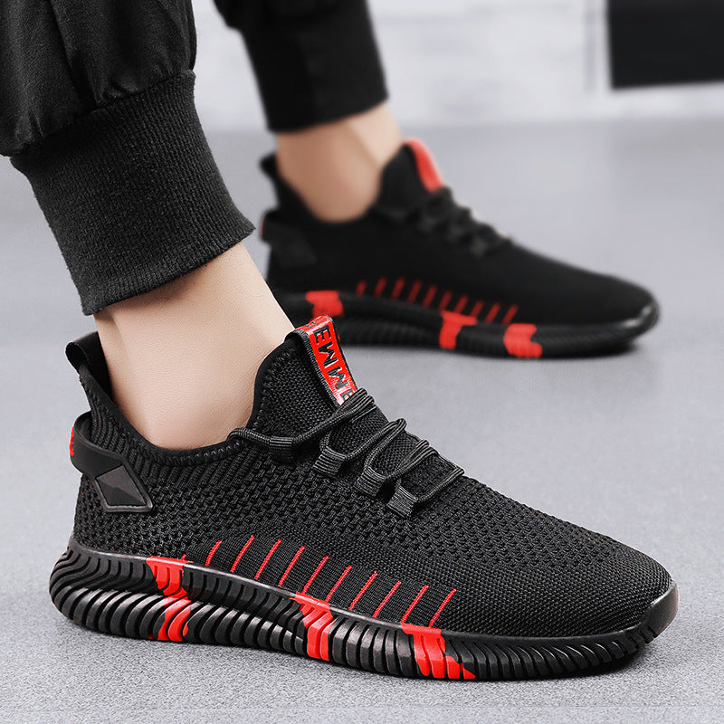 A person wearing black knit athletic sneakers with red accents and a red pull tab labeled 'FASHION', shown against a light gray studio background.