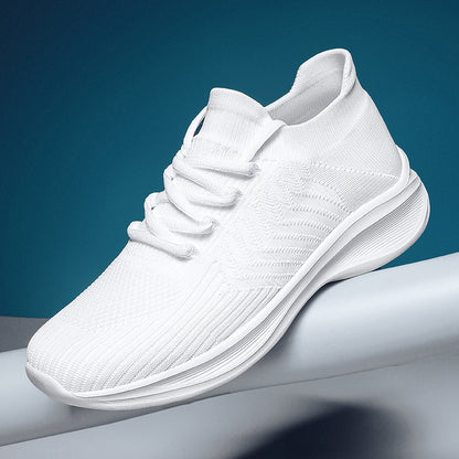 A white knit slip-on sneaker with thick white laces and a chunky white sole, resting on a white cylindrical surface against a dark teal-blue background.