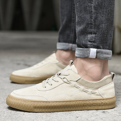 Beige sneakers with brown soles worn with rolled-up jeans on a concrete surface
