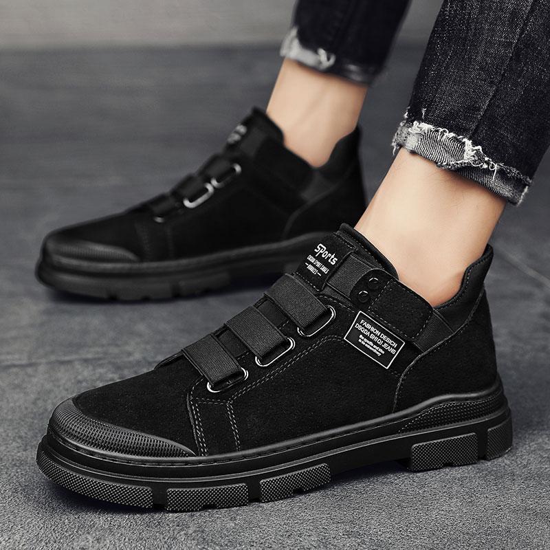 Black casual shoes with velcro straps worn by a person on a gray background