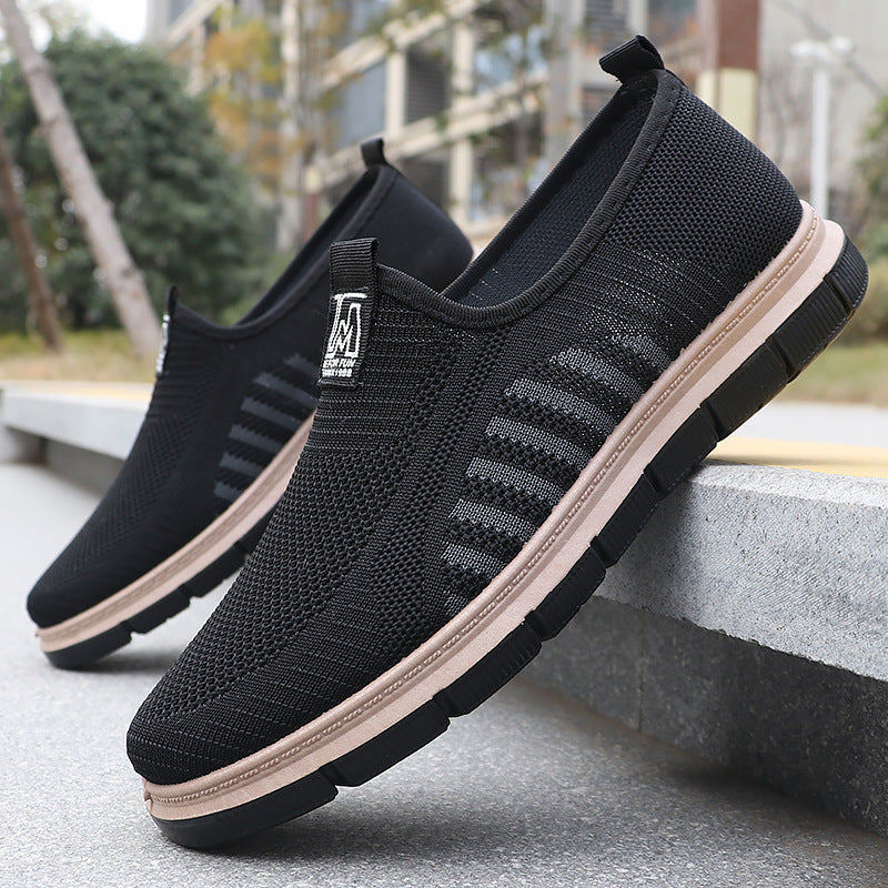 Black slip-on shoes with a beige sole on a concrete surface.