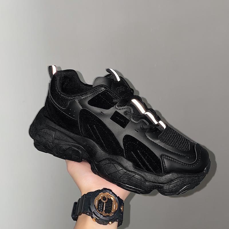 Black sneaker held in a hand with a gray background
