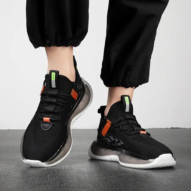 Black sneakers with orange accents worn by a person on a gray floor.