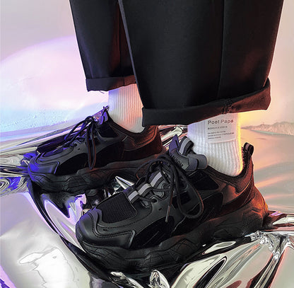 Black sneakers with white soles on a reflective surface, with a blurred background.