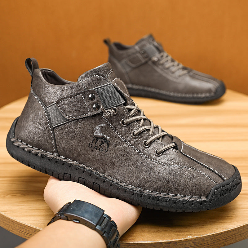 Gray leather shoes with a brand logo held by a person on a wooden surface.
