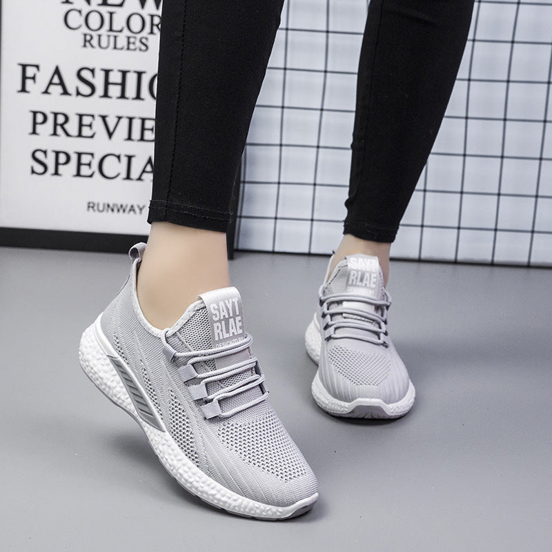 Gray sneakers worn with black pants on a gray floor.