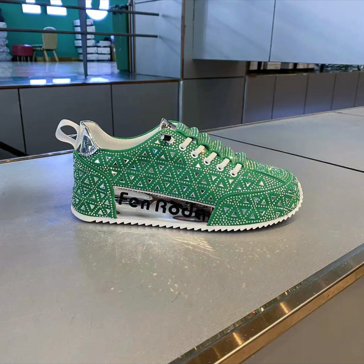 Green sneaker with intricate patterns on a metallic surface, brand 'Fen Rode' visible.
