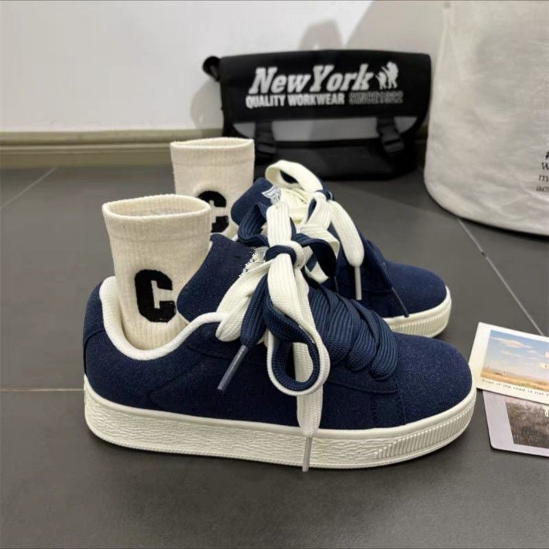 Navy blue sneakers with white soles on a gray surface, with a black bag labeled 'New York' in the background.