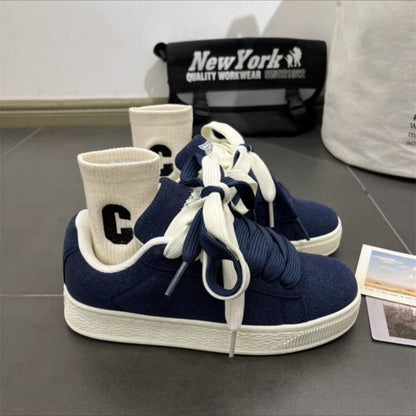 Navy blue sneakers with white soles on a gray surface, with a black bag labeled 'New York' in the background.