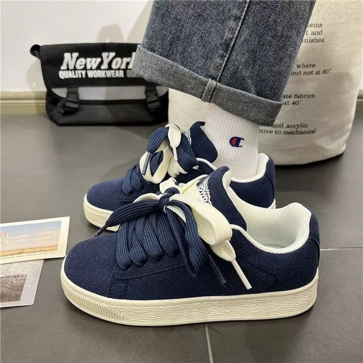 Navy blue sneakers with white soles worn with light-colored socks on a gray floor.