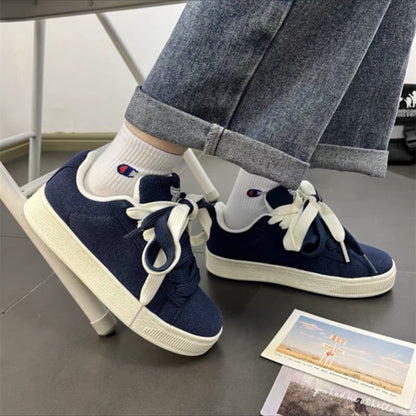 Navy blue sneakers with white soles worn with rolled-up jeans and white socks.
