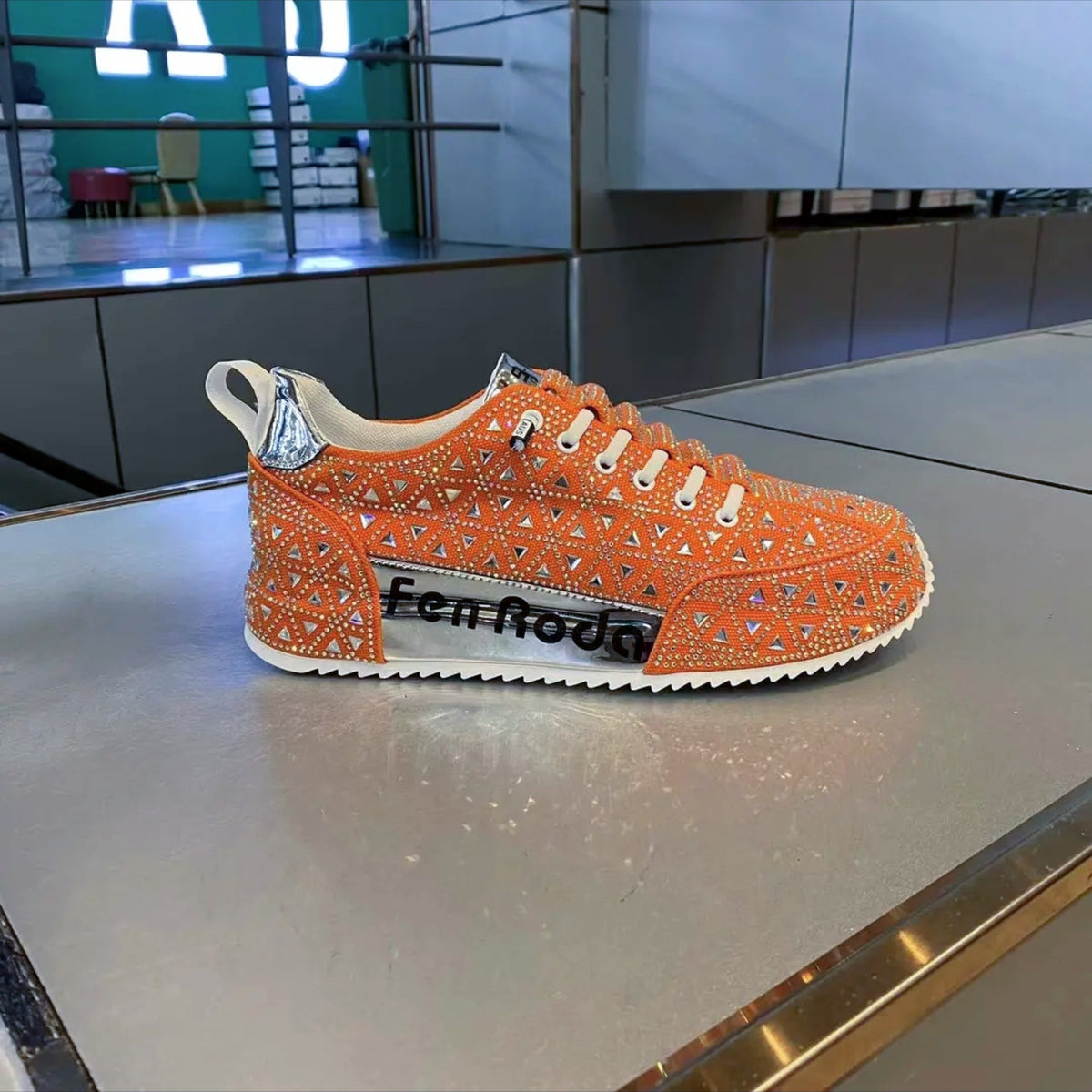 Orange sneaker with rhinestone details on a reflective surface