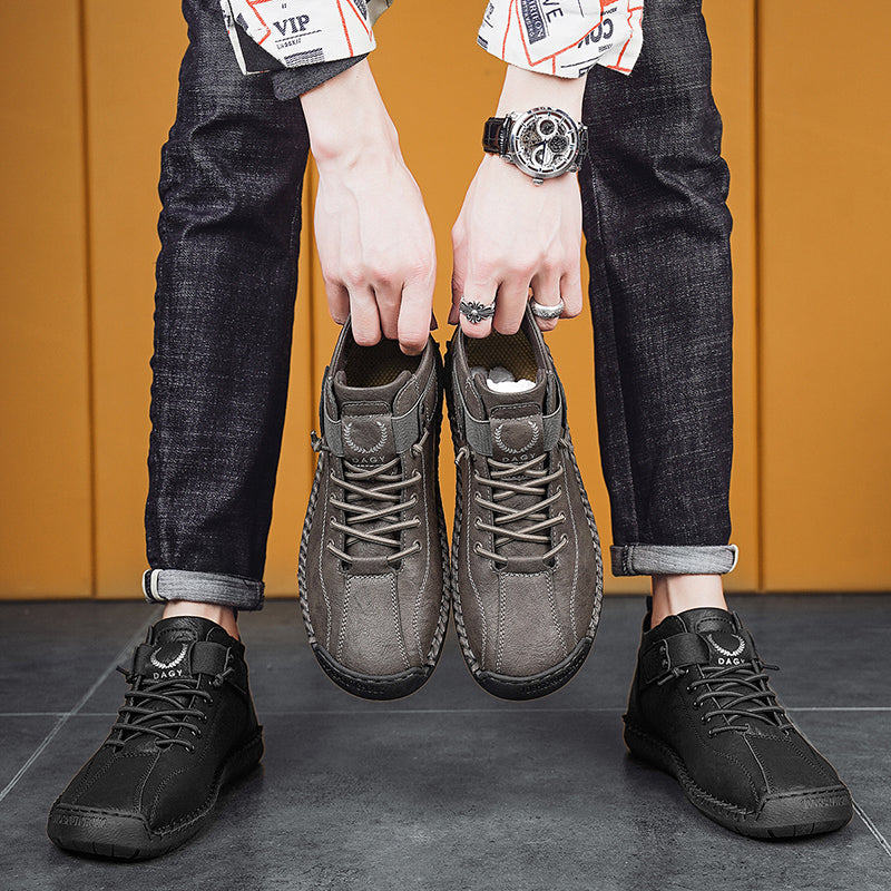 Person holding two pairs of shoes against a yellow wall.