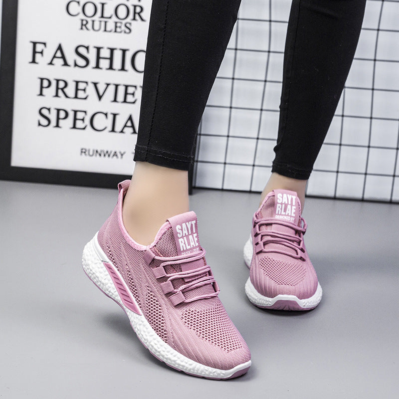 Pink sneakers worn with black pants on a gray floor.