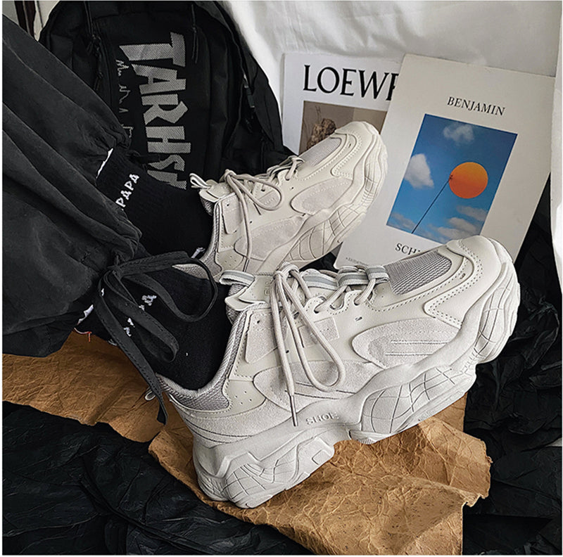 White sneakers on a surface with a black jacket, magazine, and book in the background.