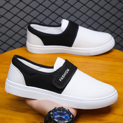 White sneakers with black straps held by a person wearing a watch on a wooden surface.