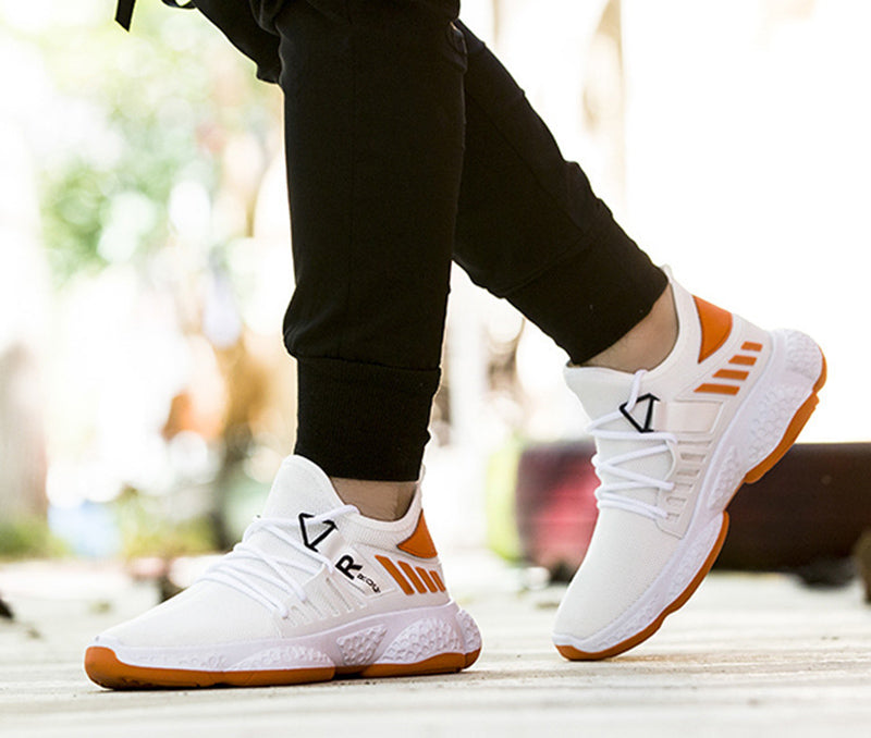 White sneakers with orange accents worn by a person sitting outdoors.